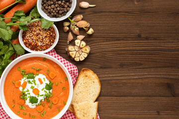 Carrot soup of freshly ground carrots with herbs and sour cream on a wooden background.