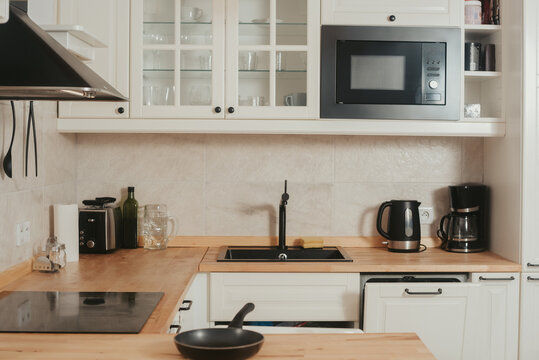Stylish kitchen, frying pan, toaster, microwave oven, extractor hood and built-in refrigerator. White kitchen design.