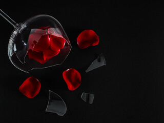 
Broken glass and rose petals with fringes lie on the left against a black background with space for text on the right, top view.