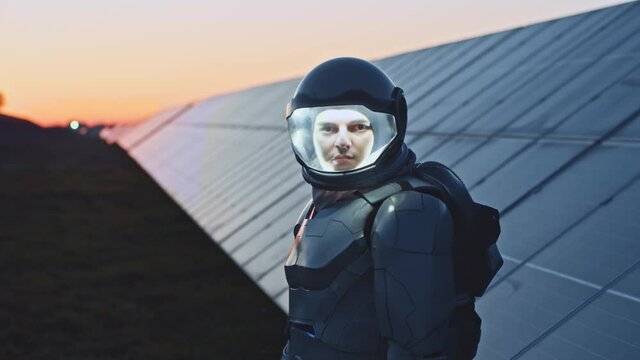 Solar field. Futuristic worker. Portrait of male astronaut employee standing near solar panels batteries for future development. Cosmonaut adjusting helmet and waving to camera. Innovations concept
