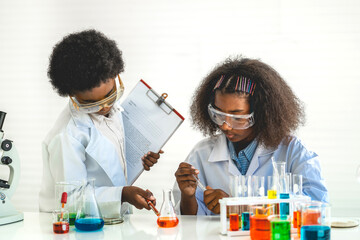 Two african american cute little boy and girl student child learning research and doing a chemical experiment while making analyzing and mixing liquid in test tube at science class on the table
