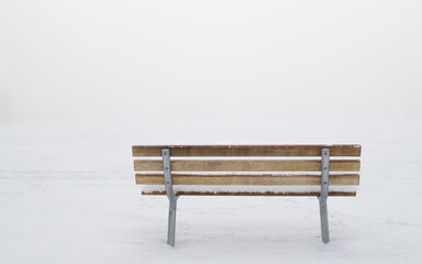 snow covered empty wooden bench viewed from behind in a ghostly winter fog with copy space