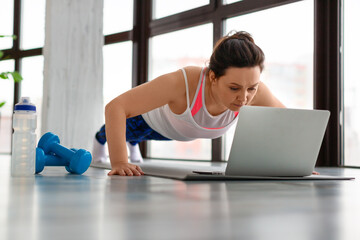 Middle-aged woman doing push-ups at home in front of a laptop monitor.