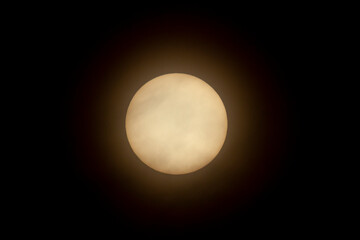 Close up isolated telephoto image of the sun in the sky taken using a super telephoto lens and a Natural Density Filter. Clouds are  seen in front of it.