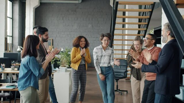 Slow motion of carefree employees male and female dancing having fun in modern open plan office. Corporate party and businesspeople concept.