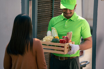 Home delivery service during covid19, Asian deliver man  in green uniform delivering fresh vegetables and Food ingredients to customer at home.