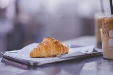Croissant on paper with tray beside iced coffee in Coffee Shop, Soft focus shot.