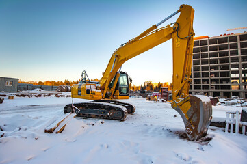 yellow excavator on the background of a new monolithic house under construction in winter