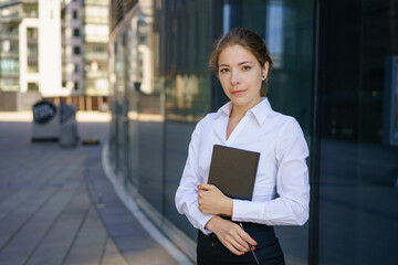 Young business woman with notepad in hand near office building