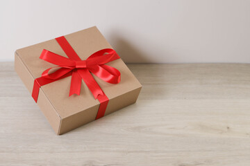 Brown gift box and red ribbon on wooden background with space