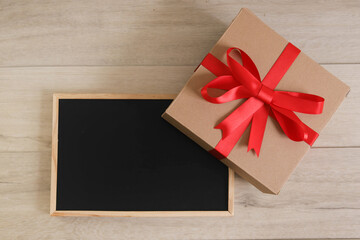 Brown gift box with red ribbon and blackboard on wooden background