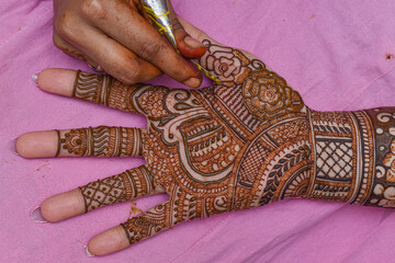 artist applying henna tattoo on women hand.Close up shot of mehndi (traditional Indian decorative art)during wedding