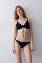 Fototapeta premium snap shot of pretty model in black lingerie on white background with red hair 