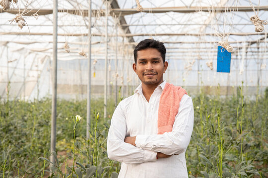 Portrait of young happy indian farmer standing cross arms at his poly house or greenhouse, agriculture business and rural prosperity concept. man wearing white cloths, copy space
