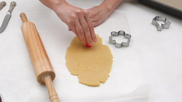 Flower shaped shortbread cookies filled with raspberry jam recipe. Chef making holes in cookie center 
