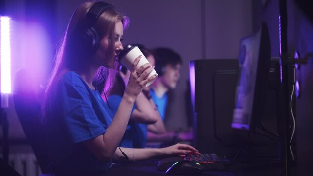 Group of friends sitting in the gaming club and having an online gaming tournament - woman drinking coffee from the cup