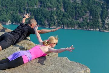 A young couple with arms outreached as they peer over the edge of the cliffs at Pulpit Rock in Norway