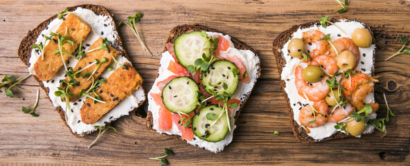 Variety of sandwiches for breakfast, snack, appetizers - tempeh, salmon, prawns grilled whole grain bread sandwiches with microgreens. on a wooden background
