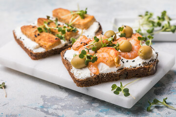 Variety of sandwiches for breakfast, snack, appetizers - tempeh, salmon, prawns grilled whole grain bread sandwiches with microgreens on a light background