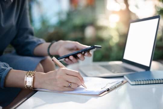 Selective Focus Of Hand Young Asian Woman Use Pen Checklist On Paperwork Of Investment While She Work From Home With Computer Laptop And Mobile Phone