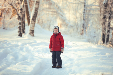 Smiling small boy in red coat in winter forest