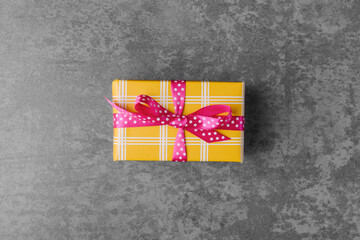 Yellow gift box with pink spotted bow on grey stone background