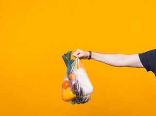 Photo of a mans hand holding a pouch with groceries near a yellow wall .