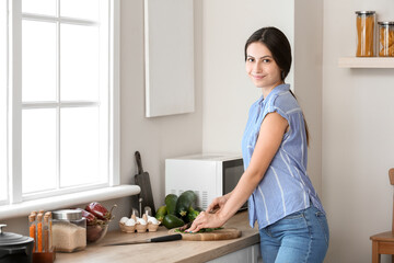 Beautiful young woman cutting parsley in kitchen