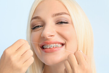 Young woman with dental braces and floss on color background
