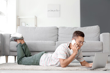 Teenage boy with laptop talking by mobile phone at home