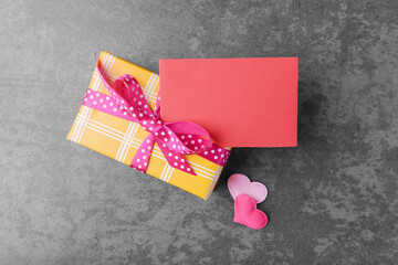 Yellow gift box, oink hearts and blank red card with copy space on grey stone background