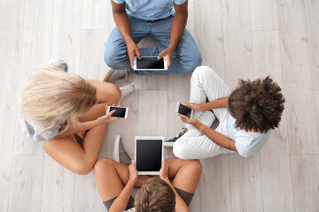 Teenagers with different devices sitting on floor, top view