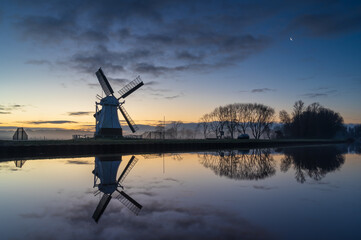 Foggy, winter dawn at a Dutch windmill reflected in a canal.