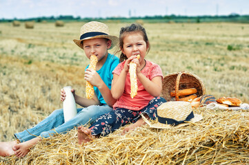 Happy children having breakfast with milk and bread in the countryside sitting on a wheat stack Happy childhood concept
