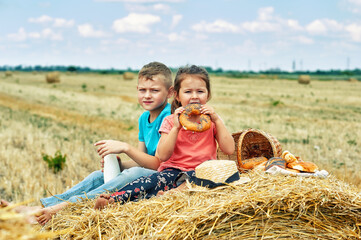 Naklejka na ściany i meble Happy children having breakfast with milk and bread in the countryside sitting on a wheat stack Happy childhood concept