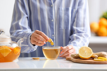 Woman making healthy tea with ginger and lemon in kitchen