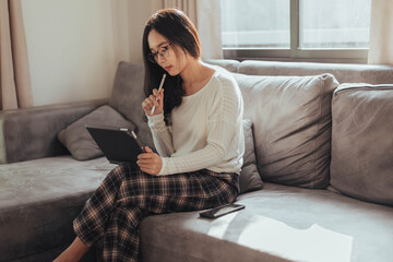 Young woman working on tablet sitting at home. Beautiful woman working at home with tablet. Working at home  during Coronavirus or Covid-19 quarantine.