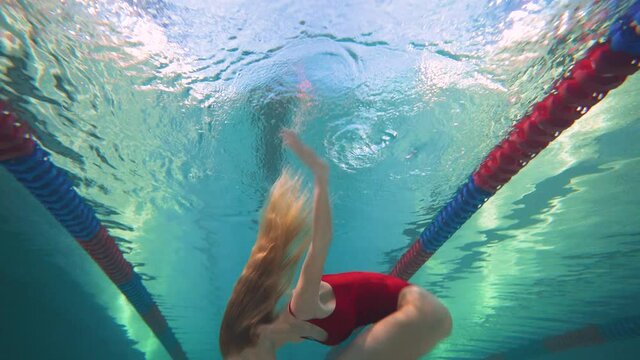 Professional female swimmer, young woman in a red bathing suit perform the elements of synchronized swimming, beautiful dance under water.