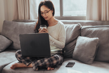 Young woman working on laptop and drinking coffee at home. Beautiful busineeswoman working at home and take a break. Working at home during Coronavirus or Covid-19 quarantine.