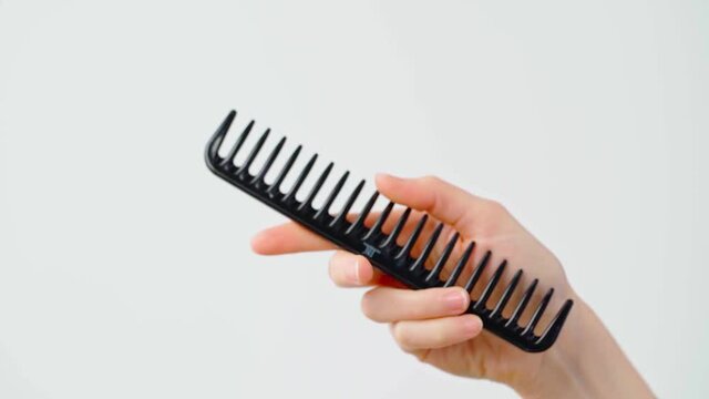 Female hand holding hair comb against white background