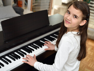 Young girl playing the piano. Child practicing on the modern electric piano at home. Music lesson. 