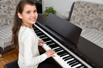 Young girl playing the piano. Child practicing on the modern electric piano at home. Music lesson. 