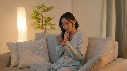 夜、ソファーでスマートフォンを見る若い女性 © polkadot