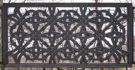 Graceful lattice of the fence with a pattern of oriental ornament in dark color against the background of winter ramtenii branches