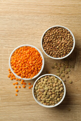 Bowls with different legumes on wooden background, top view