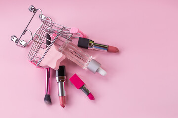 Makeup in pushcart isolated on pink background.Miniature shopping trolley cart with a set of cosmetics.For web design, postcard, banner. Buying cosmetic, online shopping concept.Copy space.