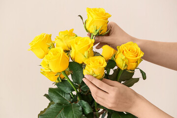 Hands with beautiful yellow roses on light background