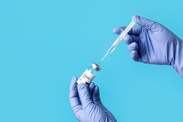 Doctor's hands with syringe and vaccine for immunization against COVID-19 on color background