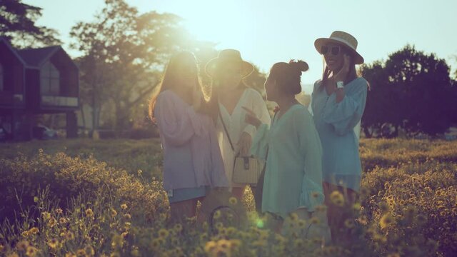sun flare light ray with group of asian female friend laugh smile joyful travel together standing conversation in yellow flower garden farm nature background ideas concept