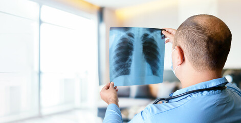 Naklejka na ściany i meble A doctor reads a chest x-ray in the bright hospital's waiting room. The concept of pneumonia, respiratory diseases. Copy space. Banner.